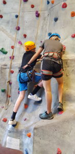 Young person learning to climb on a climbing wall with a guide