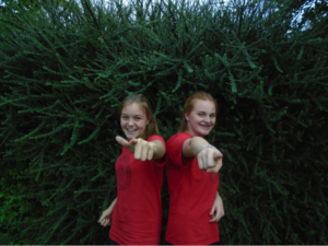Two chips team members pointing at the camera with a green bush behind them